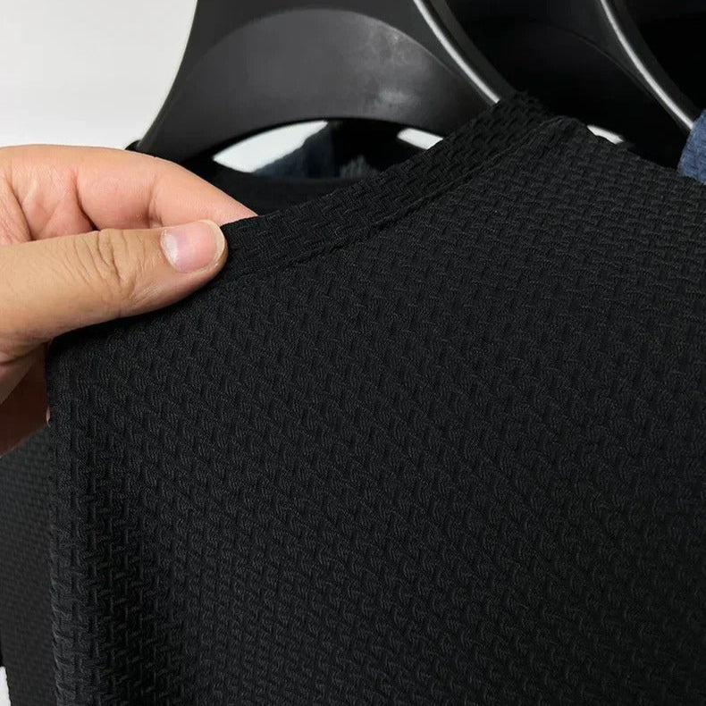 Black textured sweater being held by a hand on a hanger against a white background